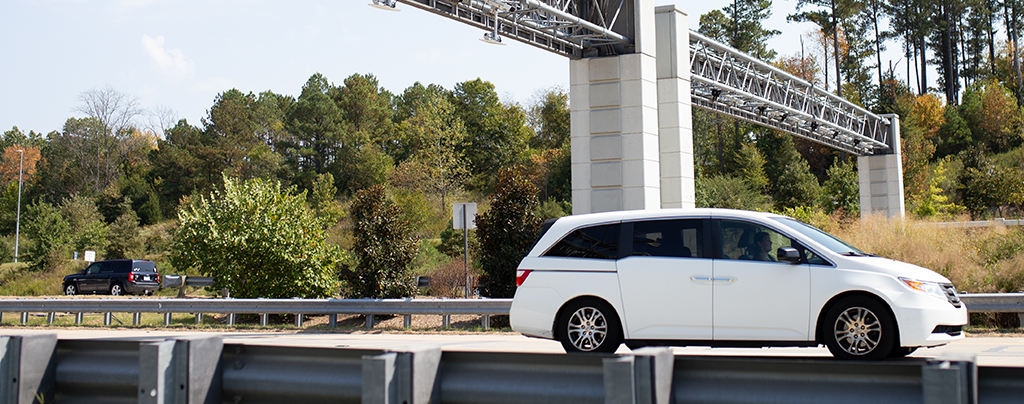 White minivan passig under toll gantry on a toll road.